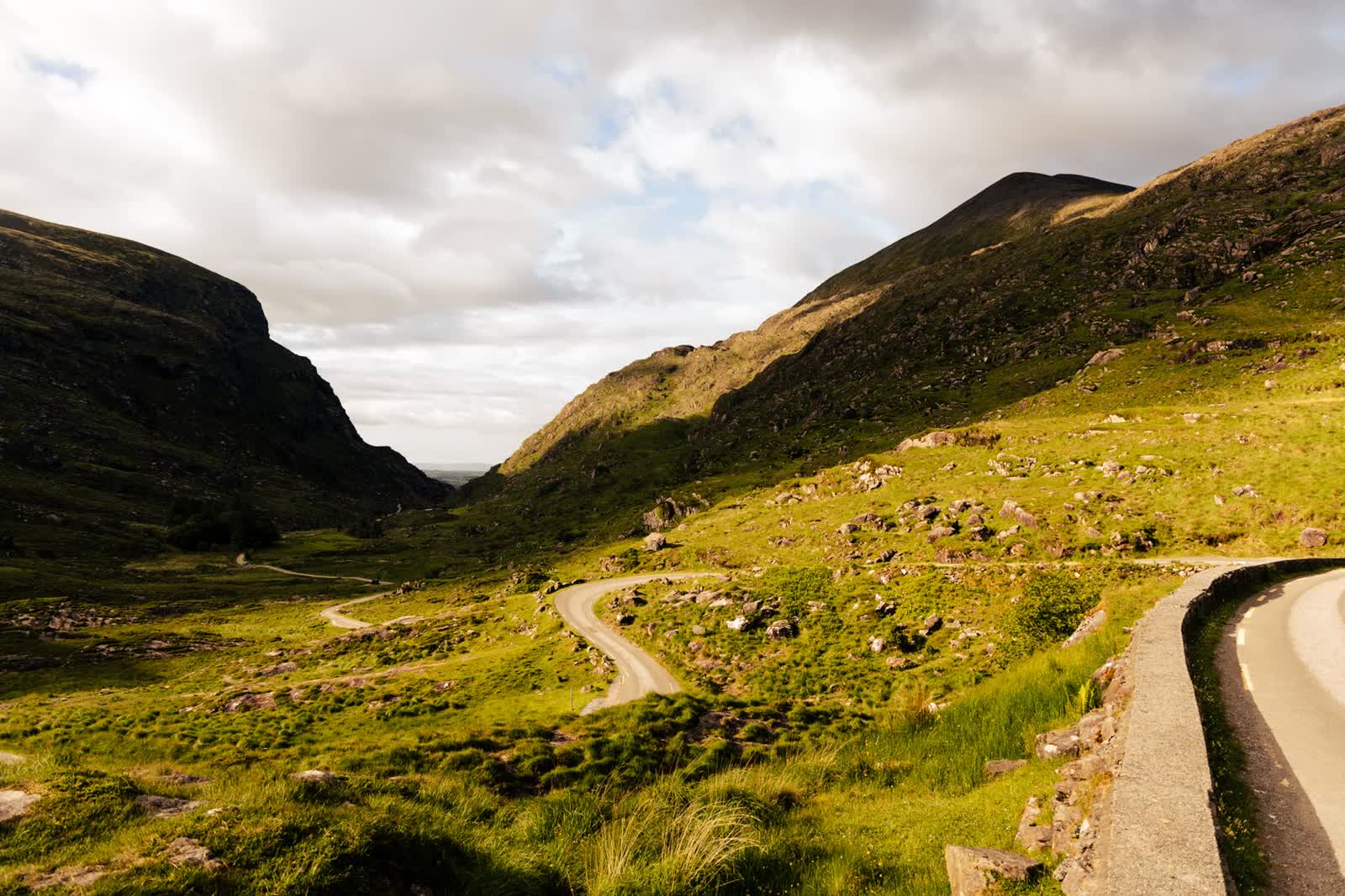 A winding country road through the green mountains of Kerry, Ireland at golden hour